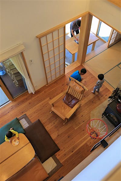 吹き抜けから見下ろすと、リビング、和室、土間サロン、ウッドデッキが連なり、2階も含めた一体空間であることが分かる。