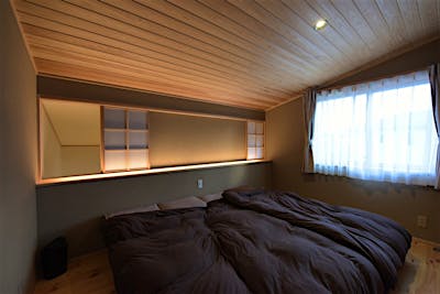 吹抜けとつながった寝室。左右対称に空気取り用の建具を配置。その建具を障子にし、通した敷居を活かして手前には間接照明をプランニング。内装の壁にはあえて京壁を使用し、ムーディーな寝室を提案しました。間接照明の明かりが吹き抜け側にもさりげなく灯るのも狙っています。 