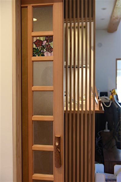 世界に一つだけの框戸。小布施出身の日本画家、中島千波さんの版画「秋明菊」をモチーフにしたデザインのステンドグラス。庭のイチイの木を利用した取っ手。 