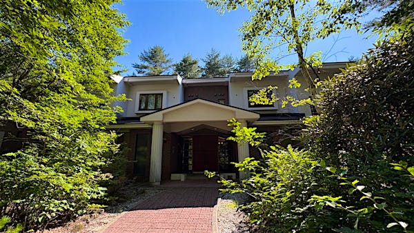 緑に囲まれたアプローチからエントランスを臨む。低層２階建てのリゾートマンション。